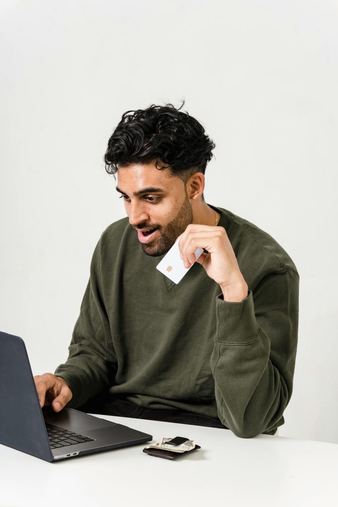 Excited man uses a laptop and credit card for online shopping indoors.